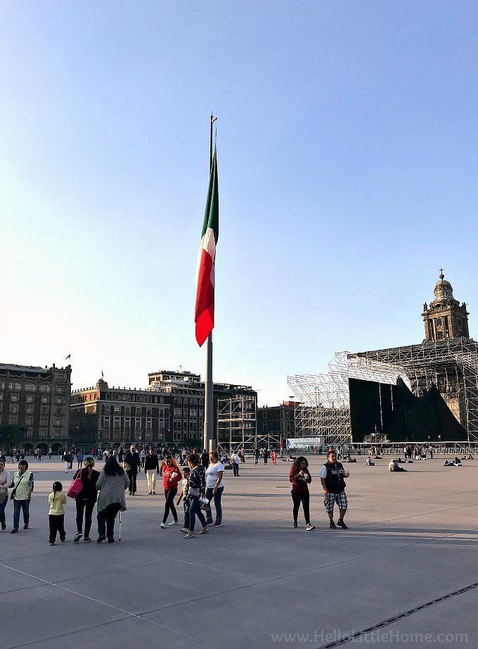 Gente de pie cerca de una enorme bandera en el centro del Zócalo.