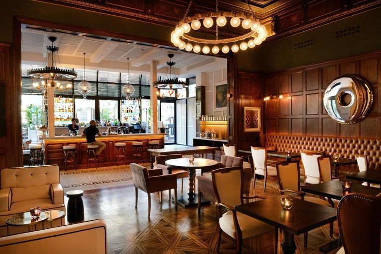 Escapada romántica a Barcelona - Los mejores hoteles 6 Un elegante comedor en el Hotel Cotton House, con modernas lámparas de araña, mesas, sillas, sillones, paredes de madera oscura y un bar
